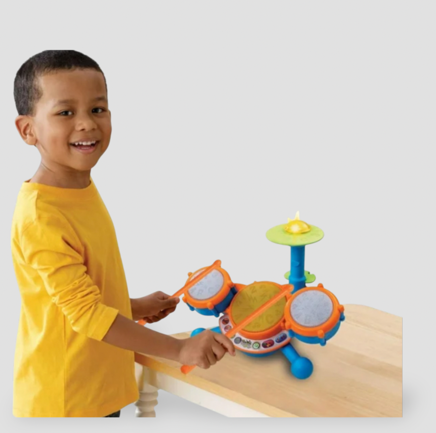 Boy in yellow shirt drumming on VTech Kidibeats kids' drum set placed on wooden table