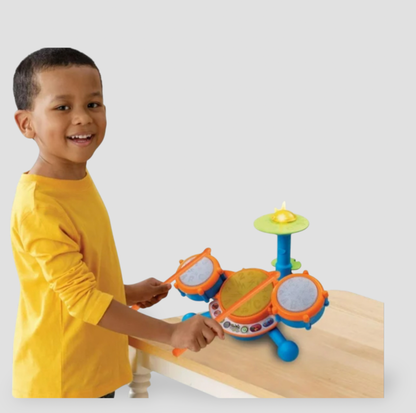 Boy in yellow shirt drumming on VTech Kidibeats kids' drum set placed on wooden table