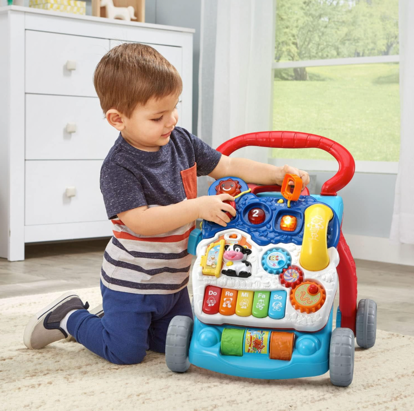 Garçonnet tournant un engrenage sur le panneau d'activités du trotteur d'éveil VTech dans une chambre d'enfant avec commode blanche