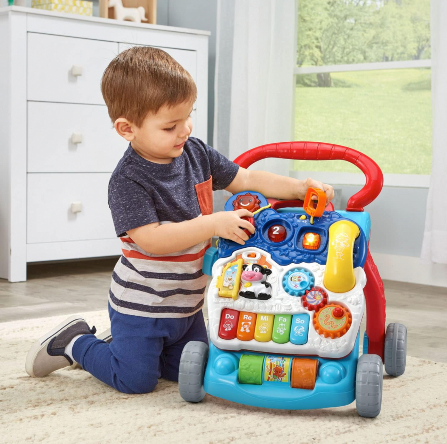 Garçonnet tournant un engrenage sur le panneau d'activités du trotteur d'éveil VTech dans une chambre d'enfant avec commode blanche