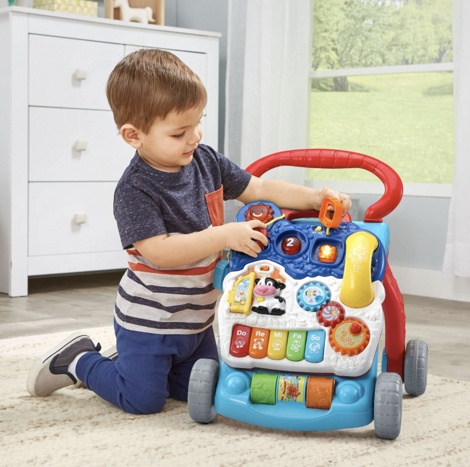 Garçonnet tournant un engrenage sur le panneau d'activités du trotteur d'éveil VTech dans une chambre d'enfant avec commode blanche