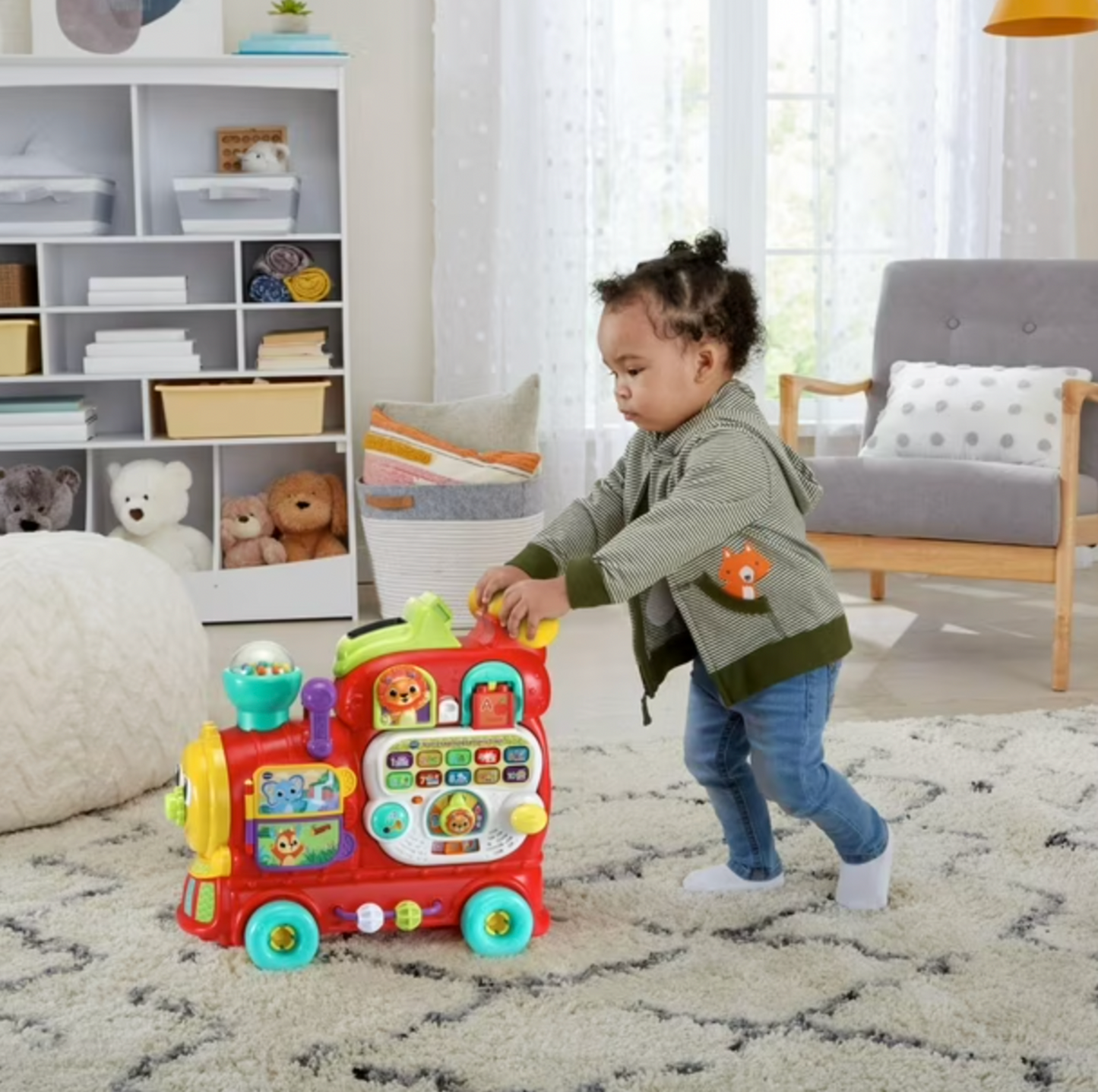 Toddler pushing red VTech ride-on letters train across white shag rug in nursery