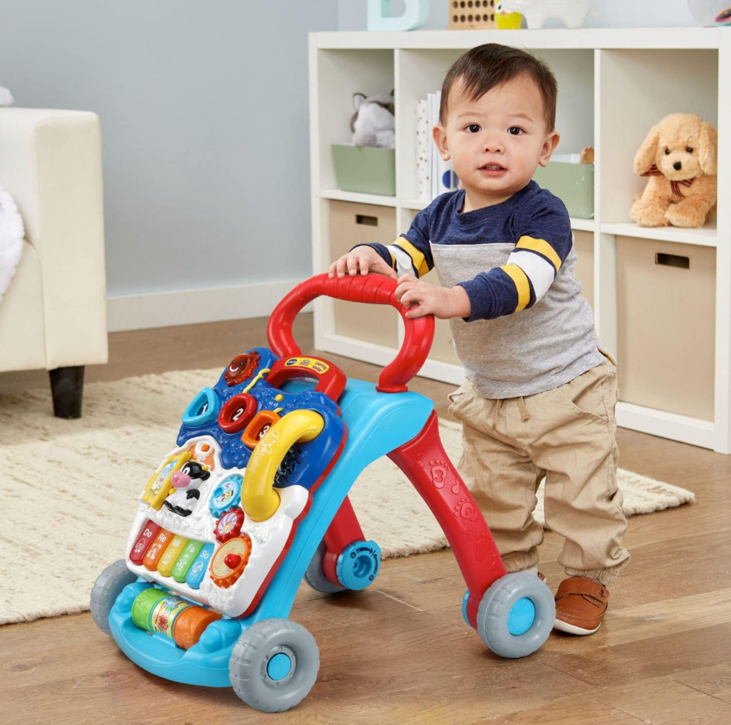 Garçonnet marchant avec le trotteur assis-debout VTech dans une salle de jeux avec rangement cubique et peluches