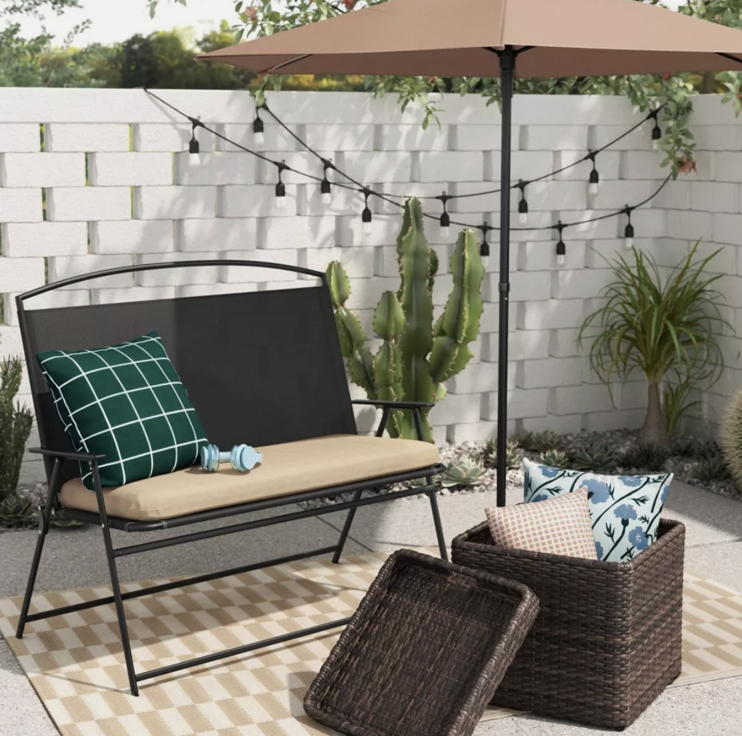 Table de rangement en osier brun avec plateau et coussins à côté d'un banc de patio noir sous parasol beige sur tapis